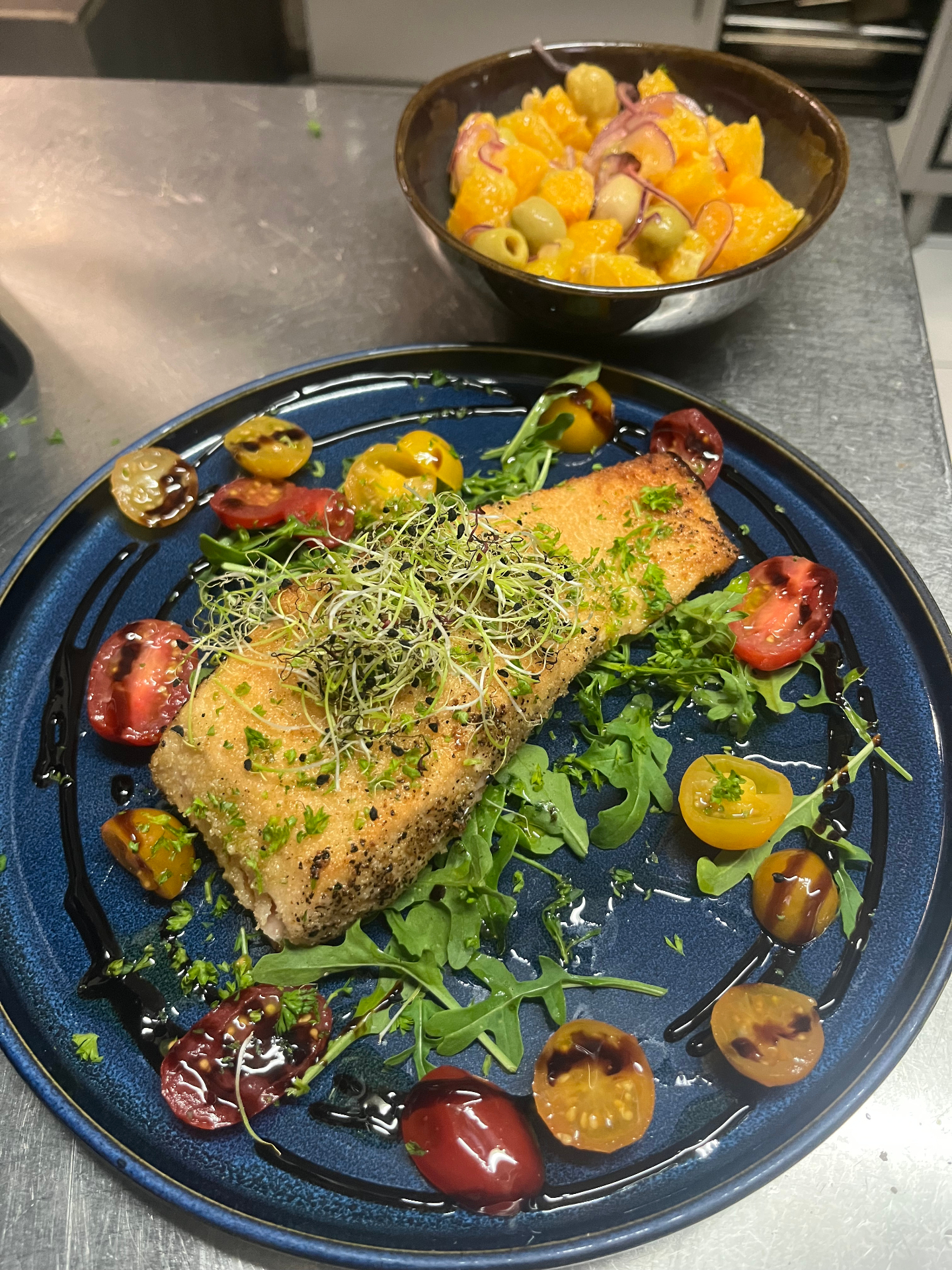 Filet de poisson pané aux graines, tomates cerises multicolores et salade d'oranges aux olives
