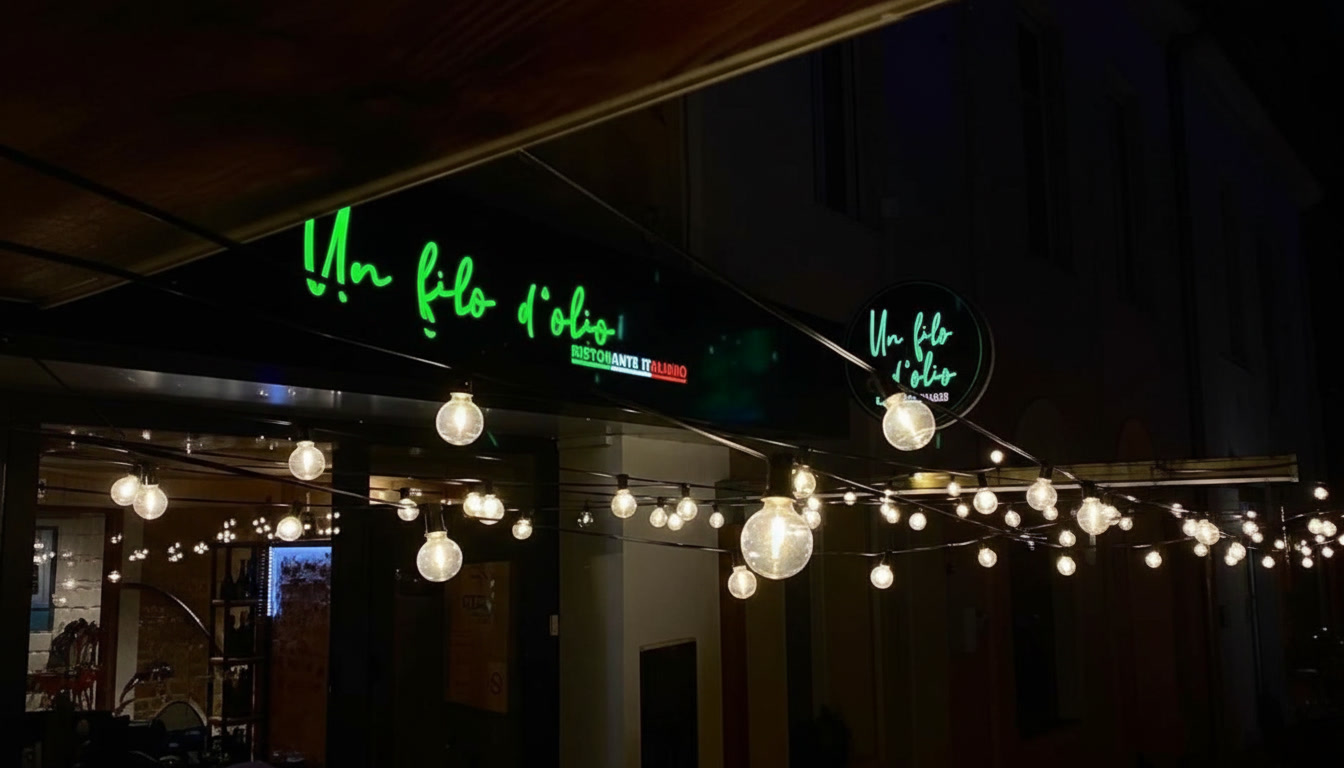 Façade de nuit du restaurant Un Filo d'Olio à Saujon, enseigne calligraphique verte et guirlandes lumineuses